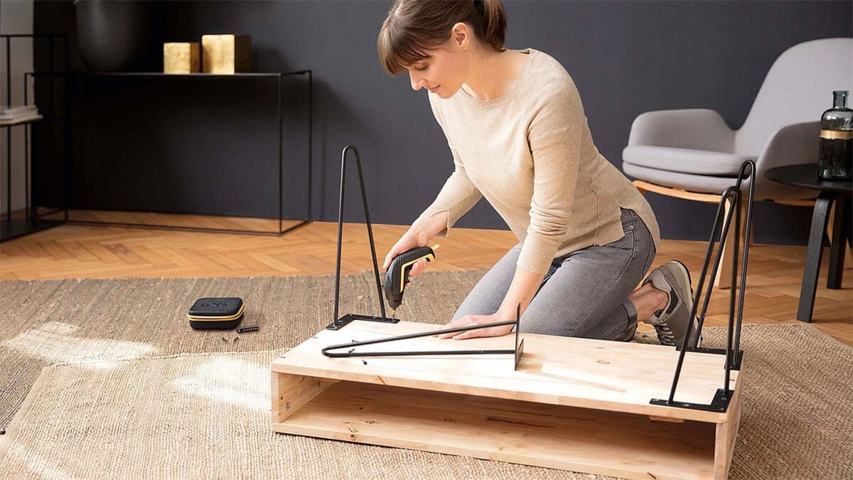 Persoană care folosește o unealtă electrică cu acumulator pentru asamblarea unei piese de mobilier